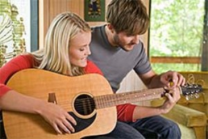 Мужчина учит играть на гитаре женщину