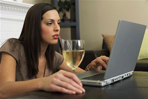 Девушка сидит за ноутбуком с бокалом вина