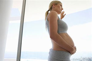 Беременная женщина стоит у окна