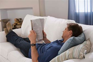 Мужчина лежит на диване и читает газету