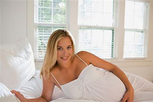 Беременная блондинка лежит на постели