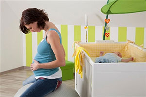 Беременная женщина сидит у кроватки