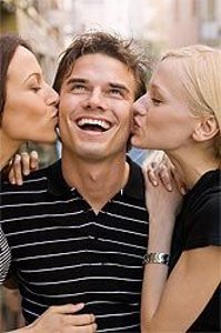 Девушки целуют улыбающегося парня