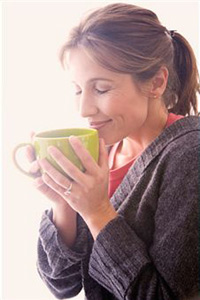 Девушка держит в руках кружку и вдыхает аромат кофе