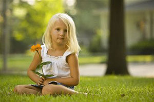 Девочка сидит на траве и держит цветок