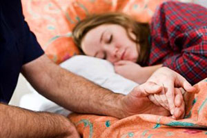 Мужчина держит за руку спящую девушку