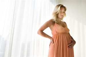Беременная женщина стоит у окна