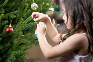 Девочка украшает елку новогодними украшениями