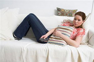 Девушка закрывшись подушкой сидит на диване