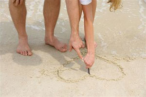 Девушка рисует сердце на песке