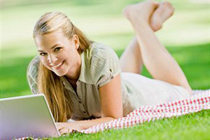 Девушка лежит на траве рядом с ноутбуком